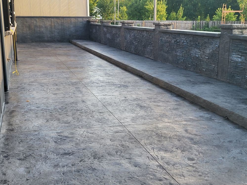 Gray stamped concrete patio with textured walls and clean lines, surrounded by greenery.